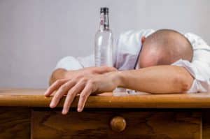 Man passing out on table with an empty bottle - sign of functional alcoholics