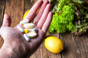 full hand of vitamins with vegetables and fruits in background