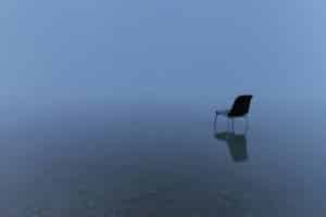 single chair reflecting water surface stormy day showing the meaning of feeling empty