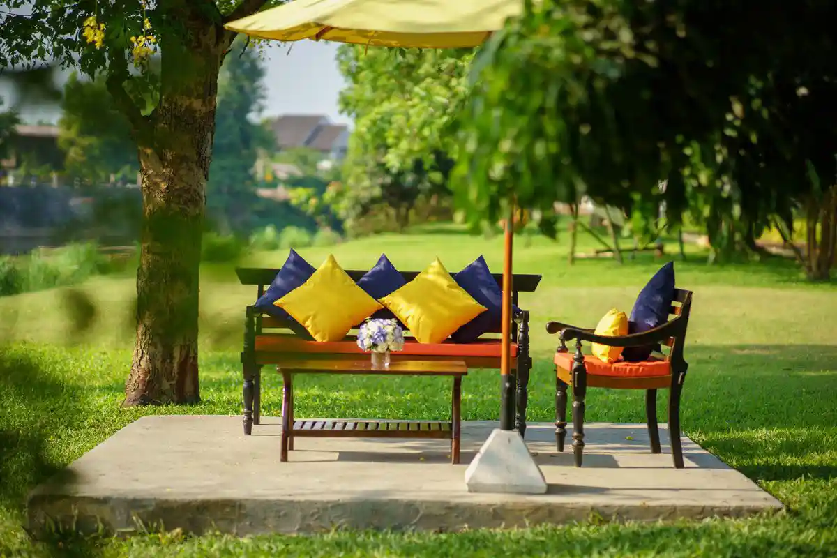 An outdoor seating area with colorful cushions on benches under a yellow umbrella, set on a concrete platform amidst a grassy garden at The Dawn.