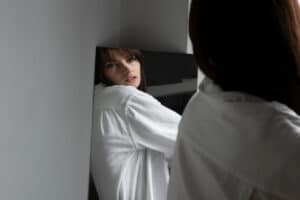 Young woman posing next to mirror creating reflection. self diagnosis.