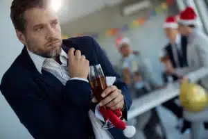A man holding a glass of drink while visibly sighing in a holiday office party