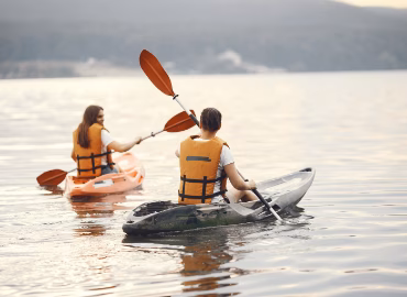 A man in a black kayak and a woman in an orange kayak paddling in a lake